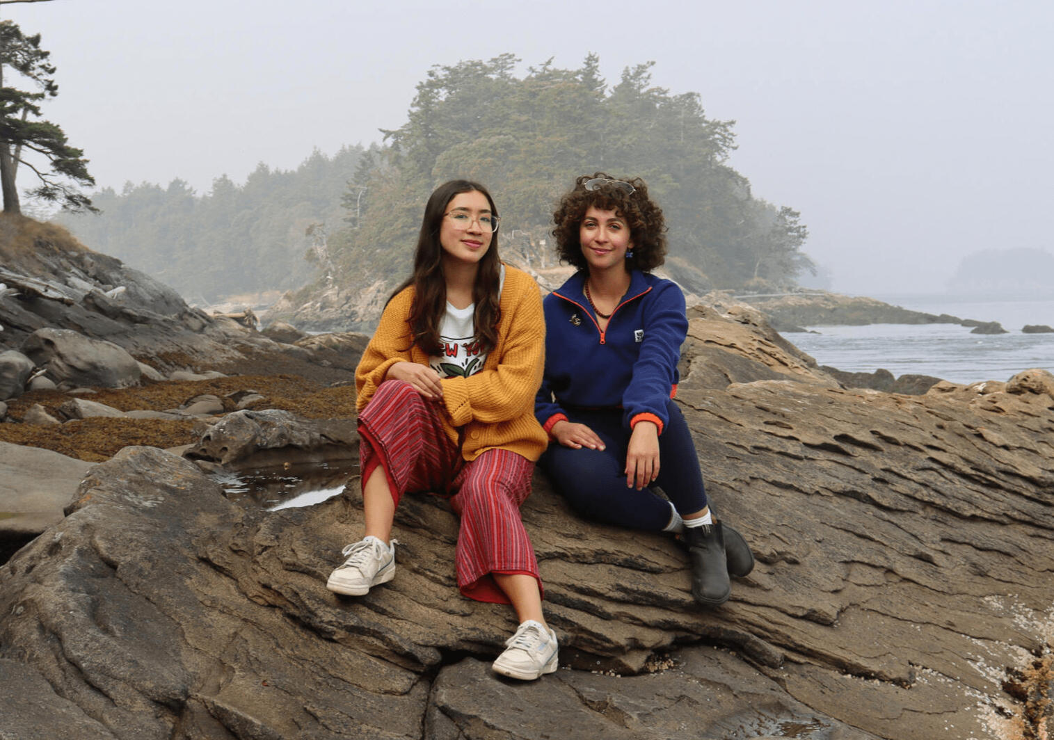 Olivia and Sofia sitting on a rocky shoreline.